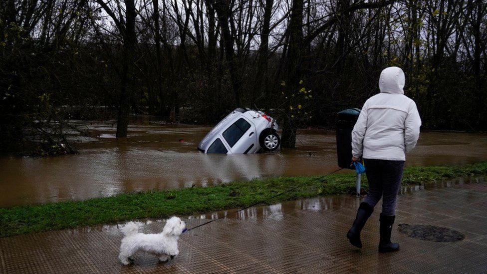A woman walks past a submerged car during floods following heavy rainfall in Villava, Spain, December 10, 2021