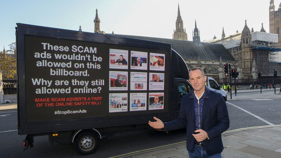 Martin Lewis poses next to a billboard showing scam advertising