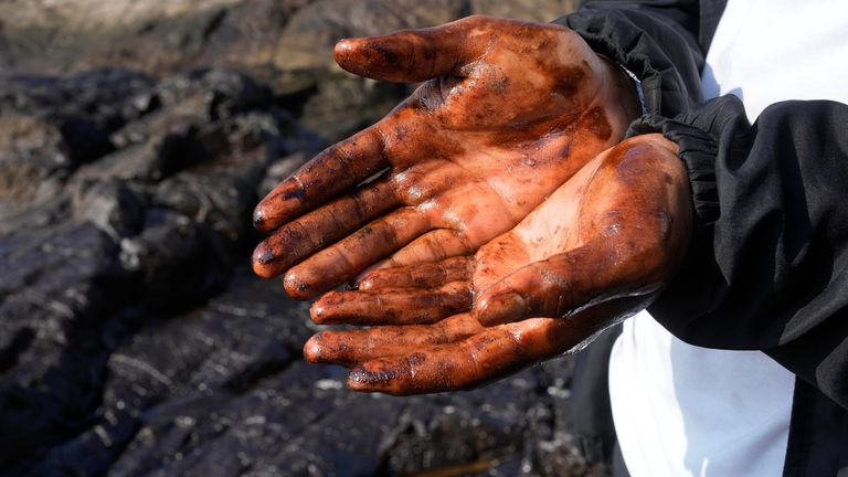 A cyclist shows his oil-covered hands after stopping to put them into the polluted water. Pic: AP